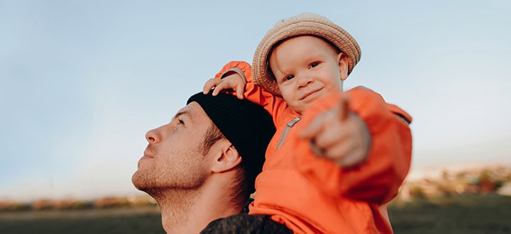 Boy on his dad's shoulders pointing at the camera