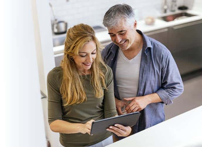 Man and woman stanind in kitchen looking at tablet.